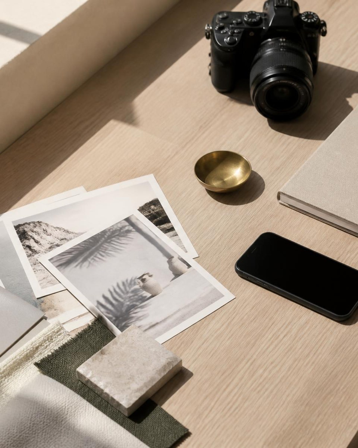 Creative studio desk with a mirrorless camera, printed mood board prints, material swatches and a brass dish in natural light